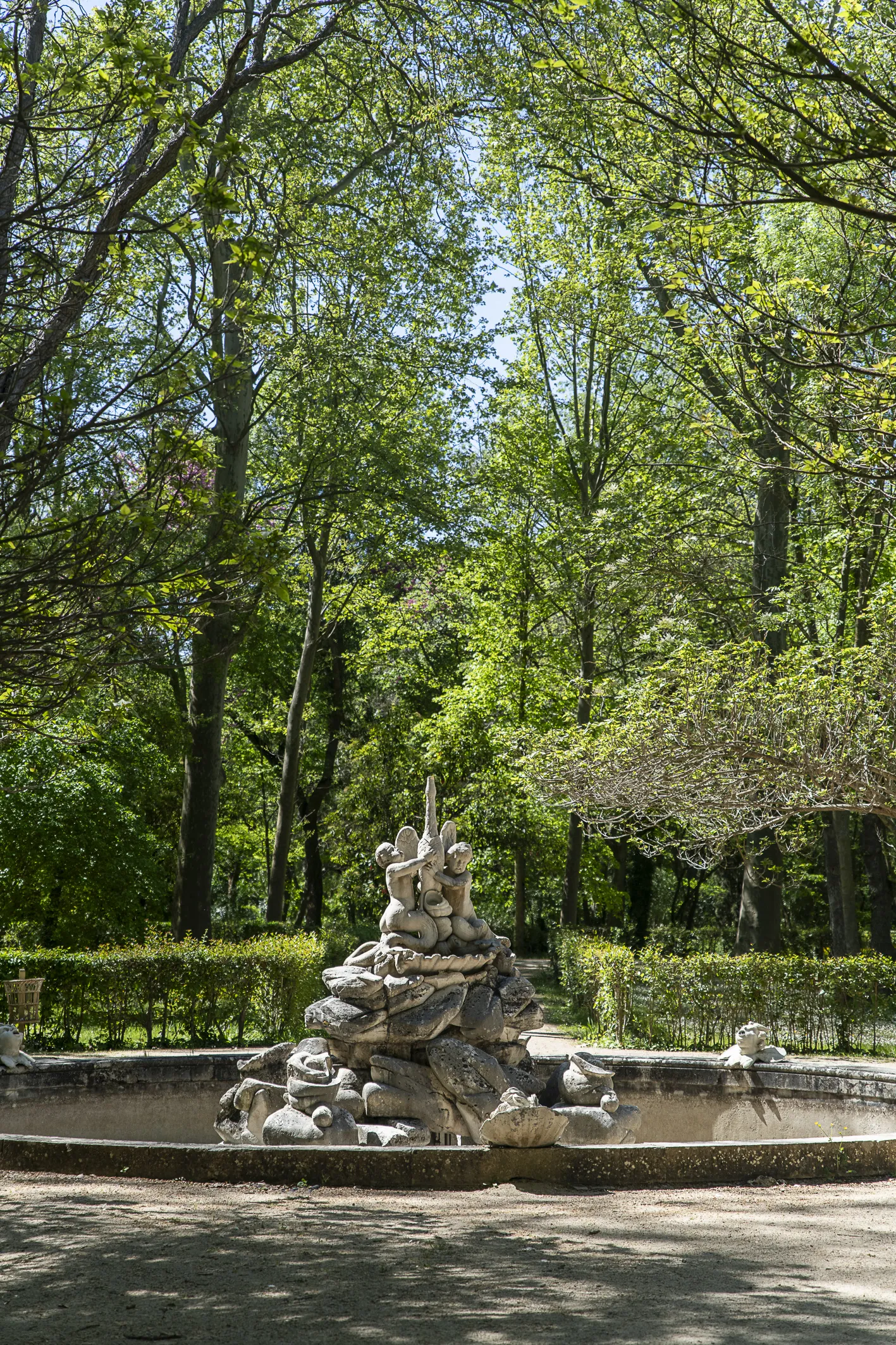 Fotografía de una fuente de piedra rodeada de arbolado verde.