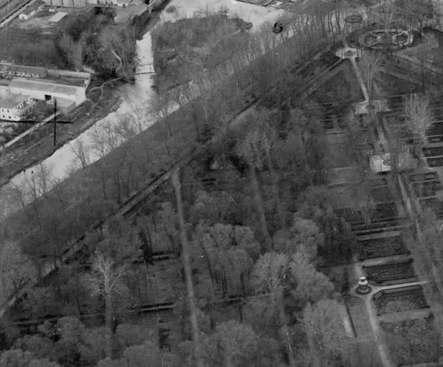 Fotografía aérea en blanco y negro de un jardín con canal de agua, arbolado y parcelas geométricas.