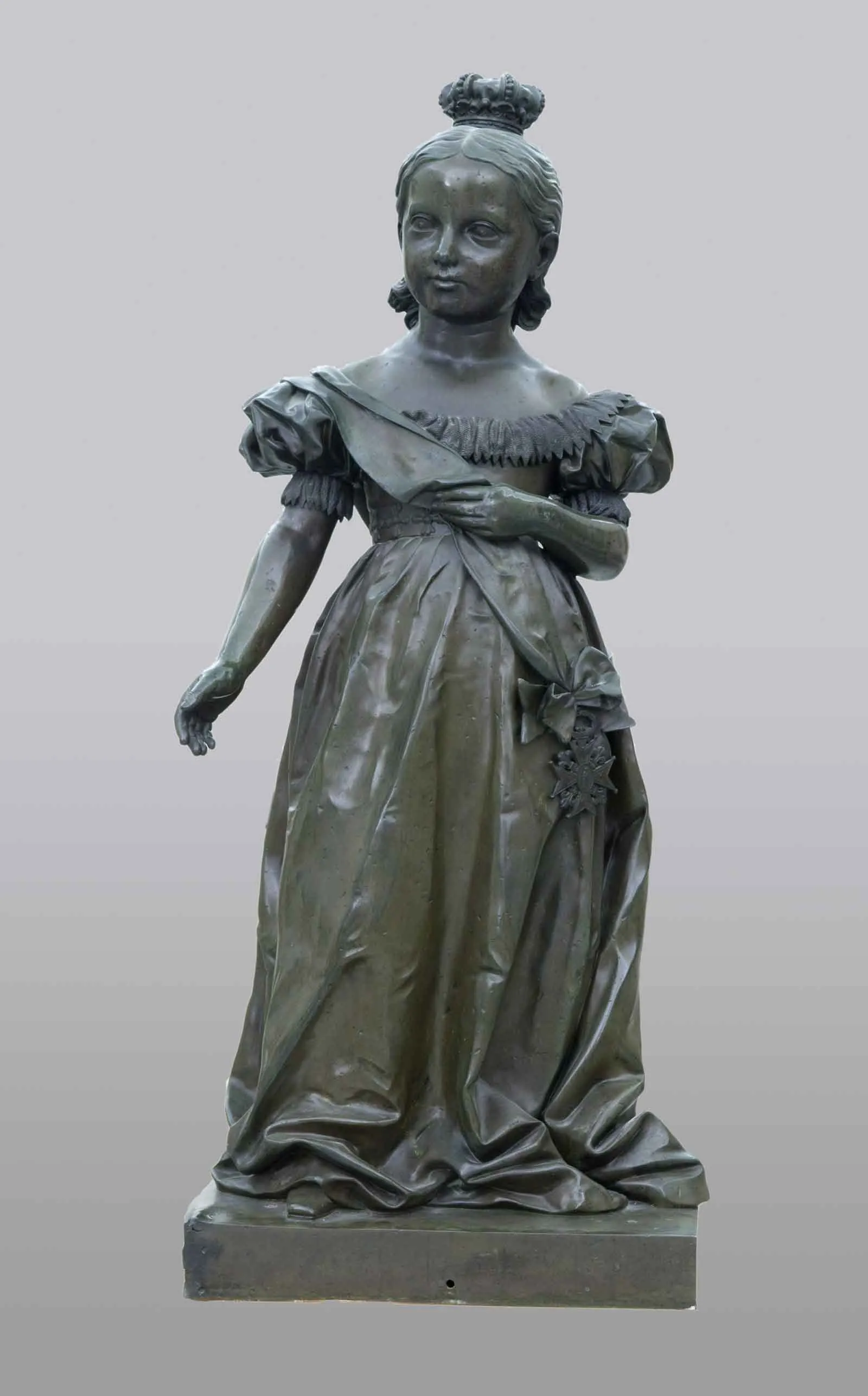 Escultura de bronce de una niña con vestido de gala, banda cruzada con una condecoración y corona sobre el pelo recogido.