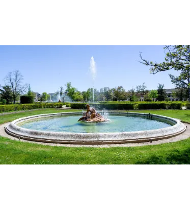 Fotografía de una fuente circular con surtidor central en una pradera del jardín.
