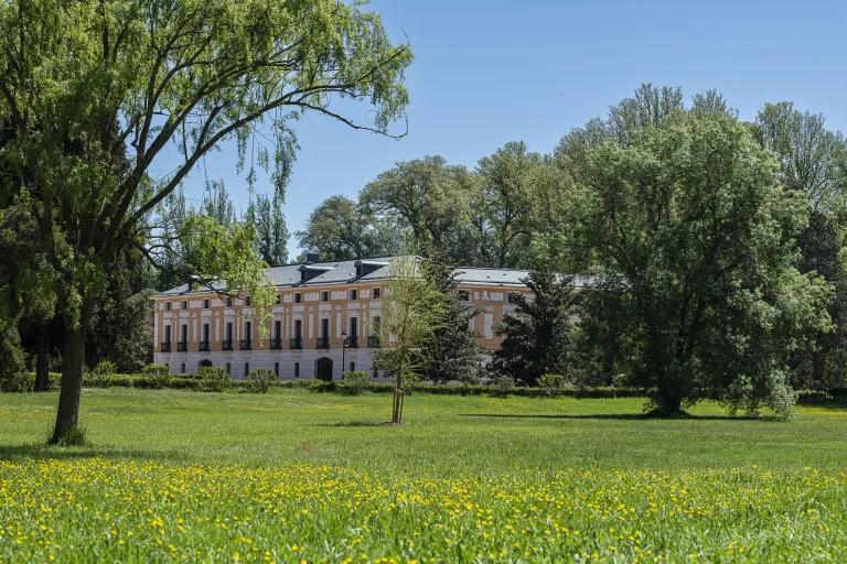 Fotografía de un palacete rosado entre arboleda y un prado con flores.