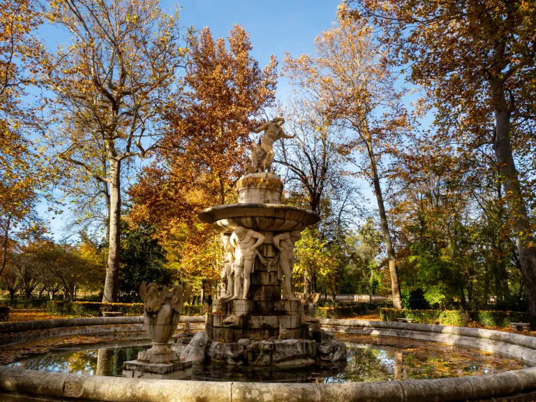 Fotografía de una fuente de piedra de varios cuerpos en el jardín, con arbolado otoñal.