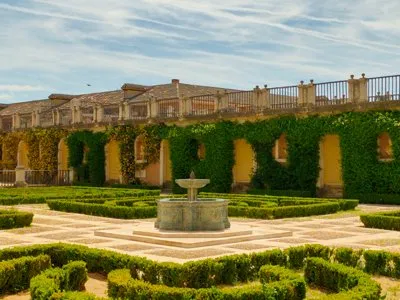 Fotografía de un jardín con fuente central, setos de boj recortados y galería porticada.