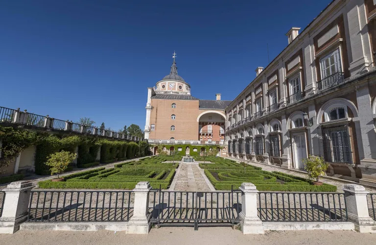 Fotografía del jardín con parterre recortado junto al palacio y su cúpula.