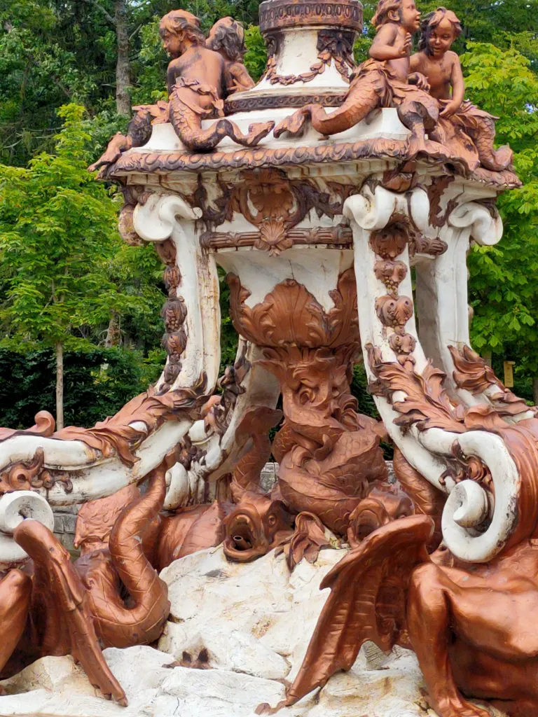 Detalle de las esculturas que decoran la fuente. En la parte superior aparecen niños tritones jugando, mientras que en la parte inferior se representan dragones alados y peces con las colas entrelazadas.