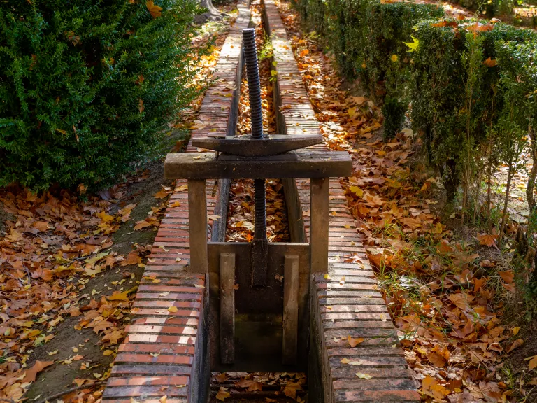 Fotografía de un canal de ladrillo con una compuerta de husillo de hierro, entre hojarasca.
