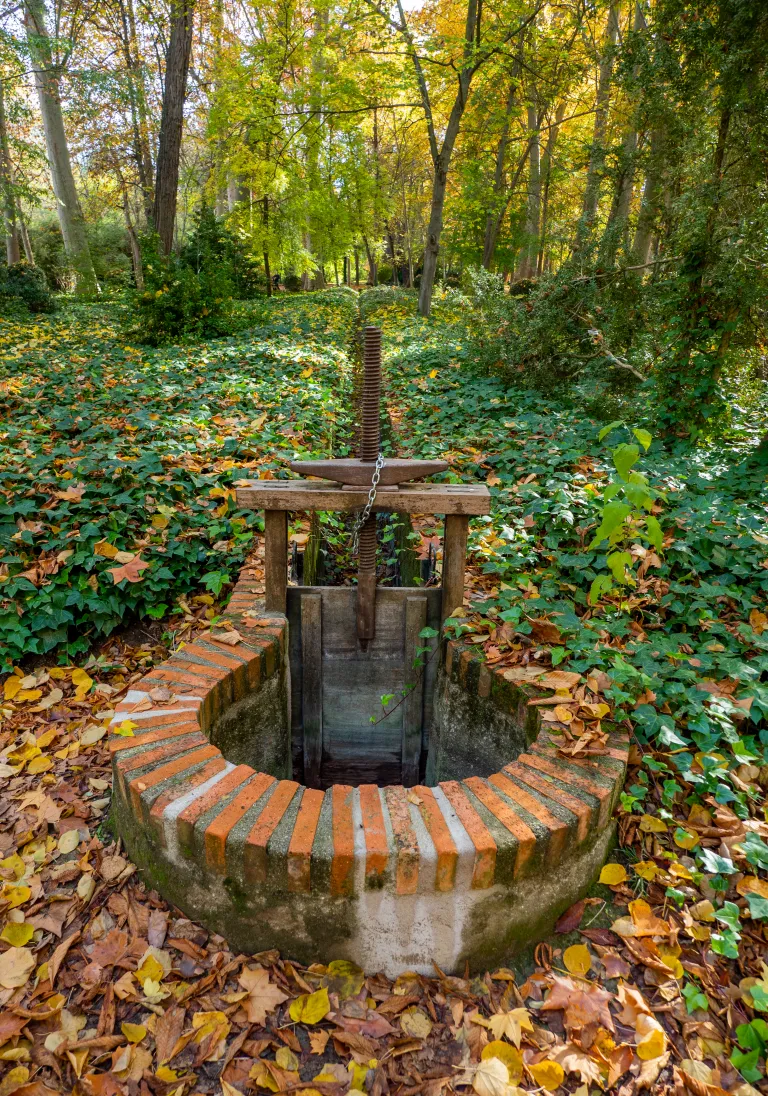 Fotografía de una compuerta circular de ladrillo con husillo de hierro en el bosque.