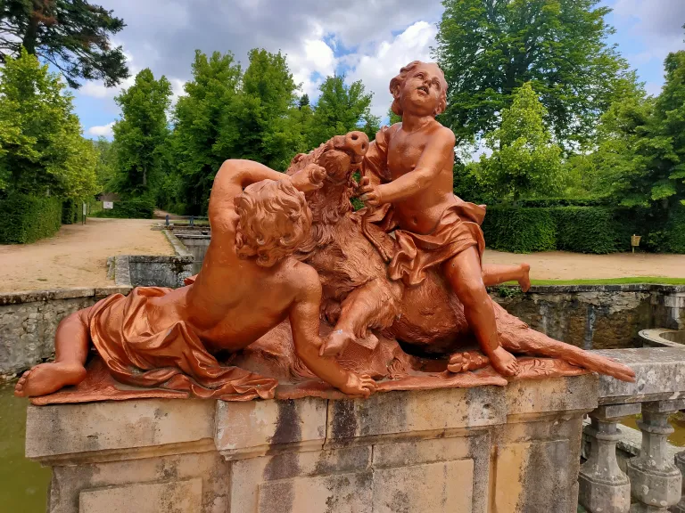 Escultura de terracota de dos niños luchando con un jabalí, uno tumbado y otro montado sobre él sujetándolo por el hocico, en un pretil de piedra.