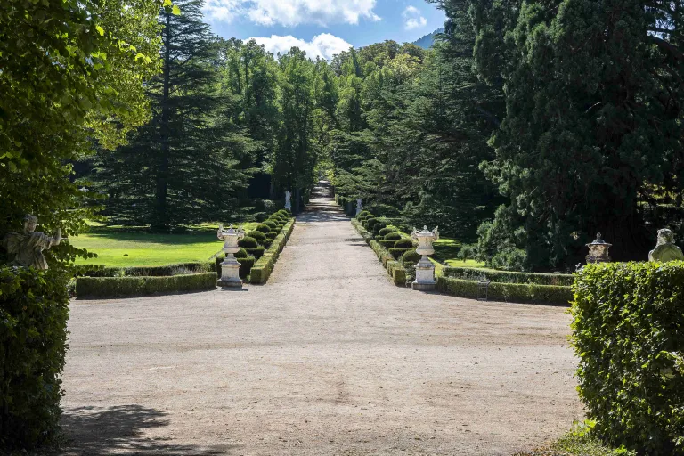 Fotografía de la vista de un jardín con un paseo central, formado por setos y adornado con jarrones y esculturas. 